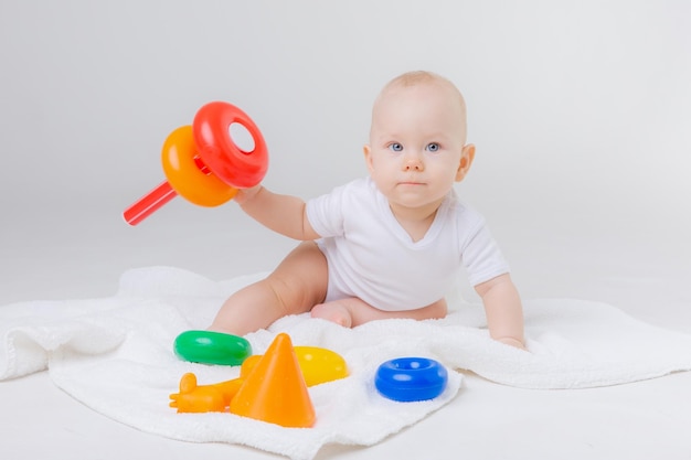 Bambino carino che gioca con la piramide giocattolo arcobaleno colorato seduto su sfondo biancoGiocattoli per bambini piccoli