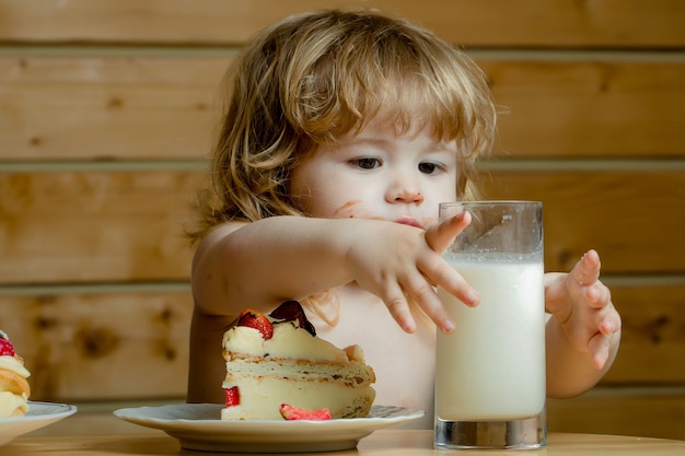 Bambino carino che mangia una gustosa torta o torta con frutta rossa alla fragola e bicchiere di yogurt