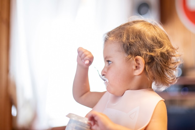 bambino carino che mangia yogurt con il cucchiaio da solo. adorabile bambino ha il pranzo. bambino affamato mangia cibo