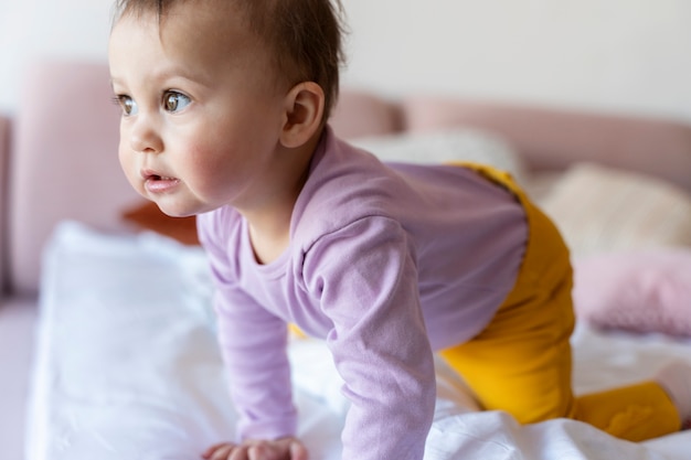 Bambino carino che striscia sul letto e sembra sorpreso