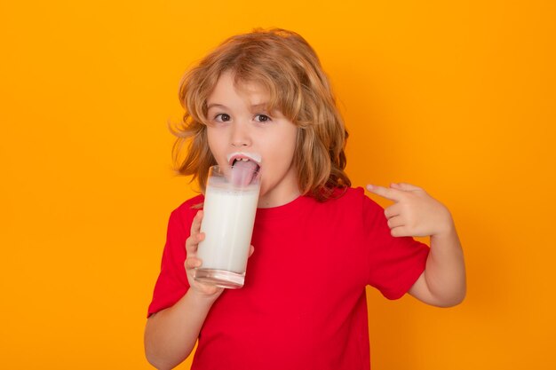 Bambino carino con bicchiere di latte su sfondo a colori da studio Bambino con baffi di latte Ritratto divertente di bambino carino con baffi di latte bianco e faccia buffa Bambino beve latte