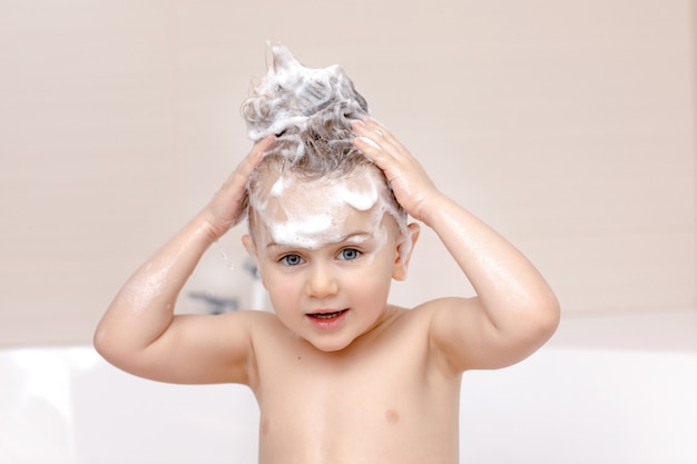 Bambino carino con schiuma shampoo sulla testa che fa il bagno e lava i capelli
