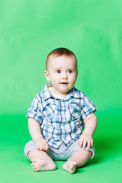 Bambino carino con una camicia a scacchi posata su un pavimento, isolata su uno sfondo verde