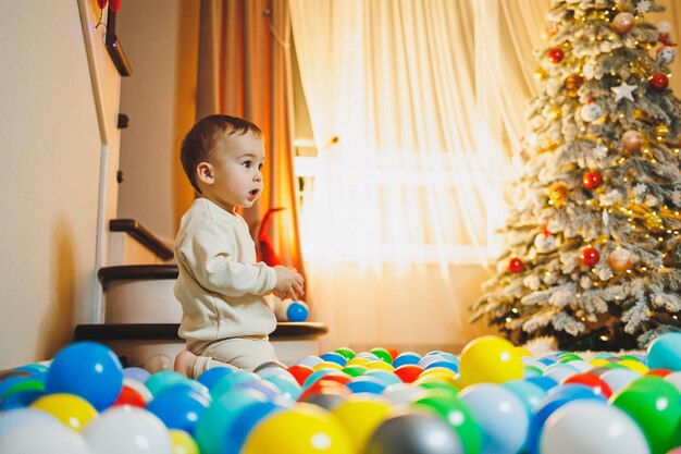 Bambino carino di 1 anno vicino all'albero di Natale seduto sul pavimento sotto l'albero nella stanza stagione delle vacanze Capodanno Natale