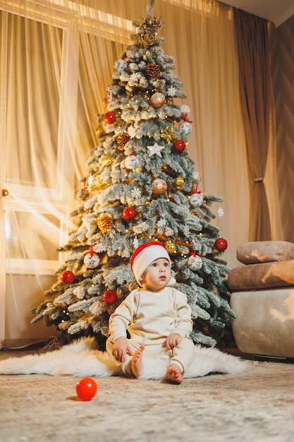 Bambino carino di 1 anno vicino all'albero di Natale seduto sul pavimento sotto l'albero nella stanza stagione delle vacanze Capodanno Natale
