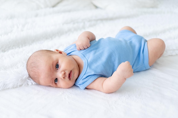 Bambino carino di tre mesi in un body blu su un letto bianco a casa