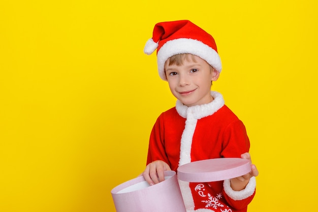 Bambino carino felice caucasico vestito da Babbo Natale che tiene in mano una scatola regalo rosa rotonda aperta.