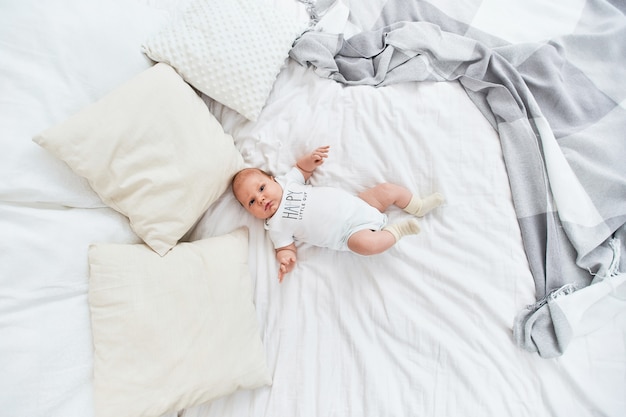 Bambino carino in tuta bianca e calze, sdraiato sulla schiena sul letto.