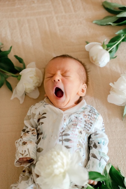 Bambino carino in vestiti stampati a fiori che giace in peonie