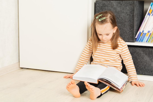 Bambino carino seduto sul pavimento e che studia un libro a casa tempo libero e istruzione a casa