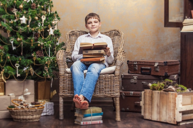 Bambino carino su una sedia che legge un libro in un interno retrò di Natale