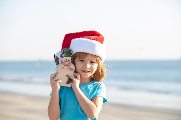 Bambino caucasico bambino babbo natale con giocattolo smowman sul mare babbo natale e pupazzo di neve in estate spiaggia concetto ...