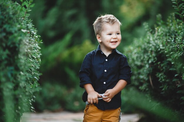Bambino caucasico bianco con un sorriso che cammina nel parco su uno sfondo di alberi verdi
