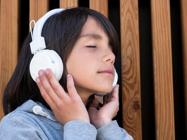 Bambino che ascolta musica con le cuffie bianche davanti a una parete di legno