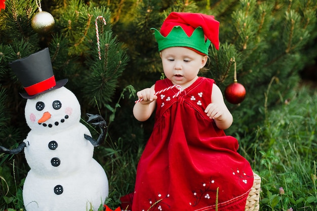 Bambino che aspetta un natale in legno a juli. il ritratto dei bambini piccoli si avvicina all'albero di Natale. ragazza che decora l'albero di Natale con le palle.