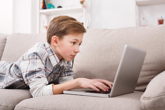Bambino che blogga in internet, ragazzo concentrato con laptop a casa