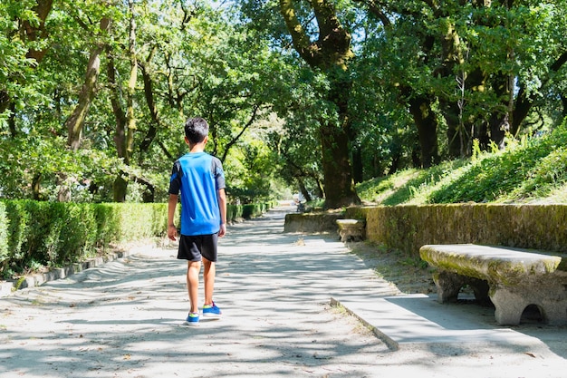 Bambino che cammina da solo in un parco cittadino in una giornata molto soleggiata.