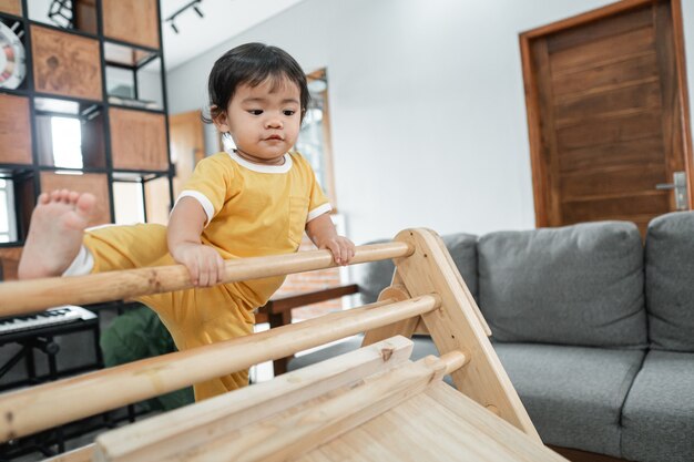 Bambino che cerca di alzare le gambe mentre si arrampica sul pikler giocattolo a triangolo in soggiorno