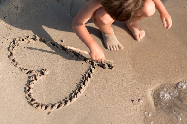 Bambino che disegna un cuore nella sabbia