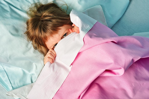 Bambino che dorme copre il viso con una coperta e non vuole svegliarsi la mattina Foto di alta qualità