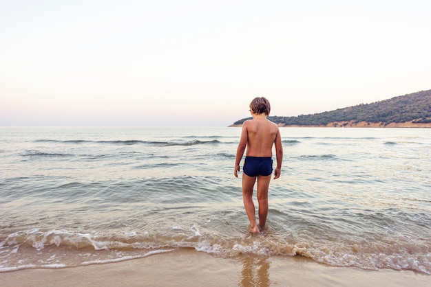 Bambino che entra in acqua di mare al tramonto