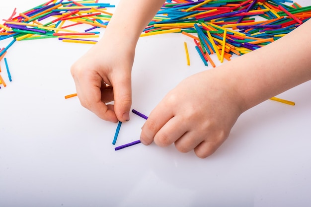 Bambino che fa forme geometriche con bastoncini colorati su sfondo bianco