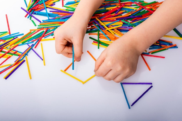 Bambino che fa forme geometriche con bastoncini colorati su sfondo bianco