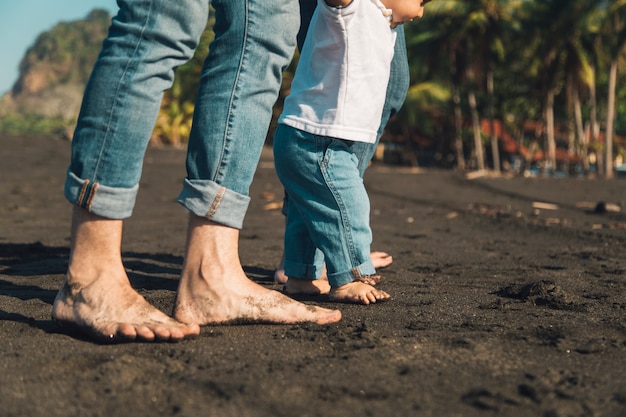 Bambino che fa i primi passi con i genitori sulla spiaggia di sabbia