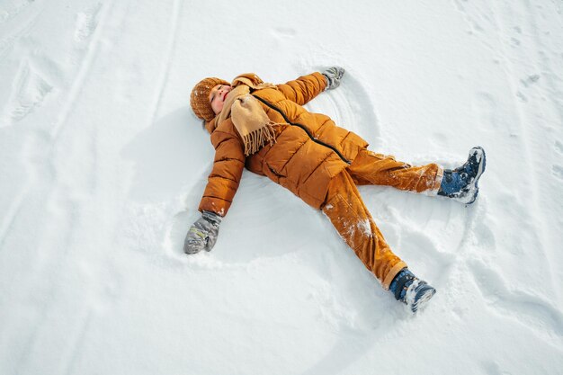 Bambino che fa un angelo della neve nel parco invernale