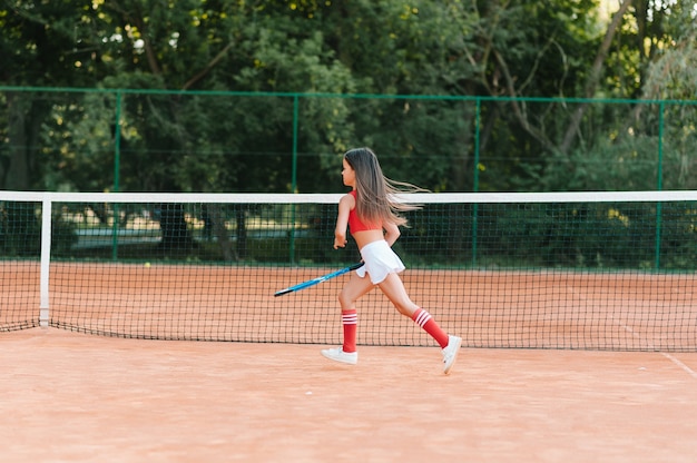 Bambino che gioca a tennis sul campo all'aperto. Bambina con racchetta da tennis e palla nel club sportivo. Esercizio attivo per i bambini