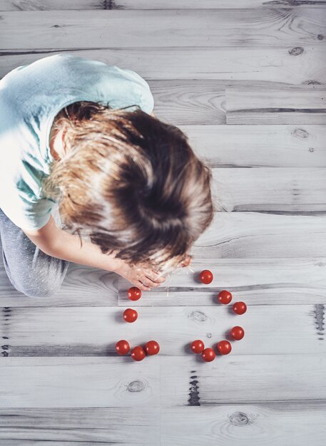 Bambino che gioca con i pomodori ciliegia su un pavimento di legno leggero da sopra