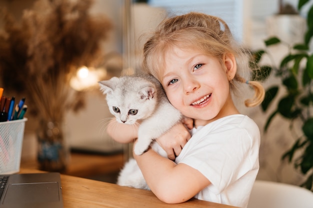 Bambino che gioca con il piccolo gatto. Una bambina tiene un gattino bianco. Una bambina si accoccola a un simpatico animale domestico e sorride mentre è seduta nel soggiorno di casa. Bambini felici e animali domestici.