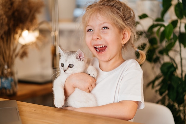 Bambino che gioca con il piccolo gatto. Una bambina tiene un gattino bianco. Una bambina si coccola con un simpatico animale domestico.