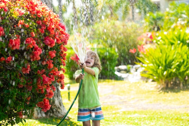 Bambino che gioca con il tubo da giardino nel cortile divertente bambino eccitato che si diverte con spruzzi d'acqua sul cortile