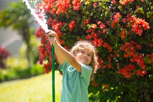 Bambino che gioca con il tubo da giardino nel cortile Divertente bambino eccitato che si diverte con spruzzi d'acqua sullo sfondo della natura del cortile Attività all'aperto per bambini estivi