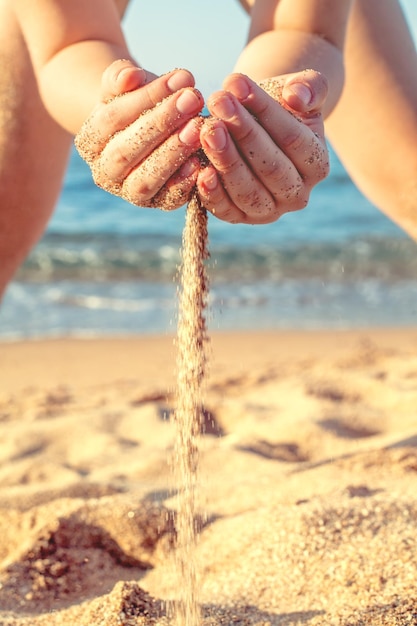 Bambino che gioca con la sabbia sul primo piano della spiaggia del mare Sabbia che cade dalle mani femminili sullo sfondo della spiaggia del mare