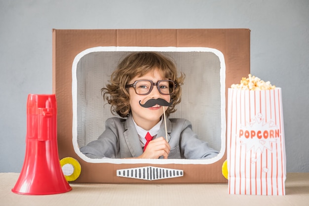 Bambino che gioca con la scatola di cartone TV. Bambino che si diverte a casa. Concetto di comunicazione