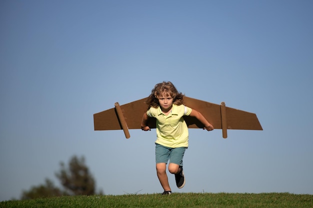 Bambino che gioca con le ali del giocattolo di cartone nel parco Concetto di giorno dei bambini Ragazzo in un costume da pilota sta giocando e sognando di diventare un astronauta aviatore Concetto di libertà dei bambini