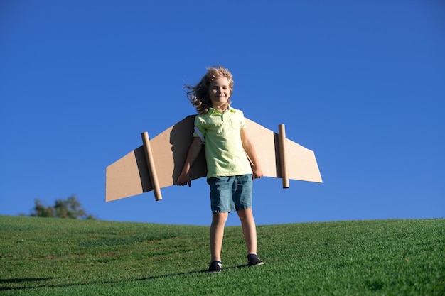 Bambino che gioca con le ali del giocattolo di cartone nel parco Concetto di giorno dei bambini Ragazzo in un costume da pilota sta giocando e sognando di diventare un astronauta aviatore