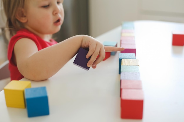 Bambino che gioca e costruisce con colorati mattoni giocattolo in legno sul tavolo di legno bianco apprendimento precoce e