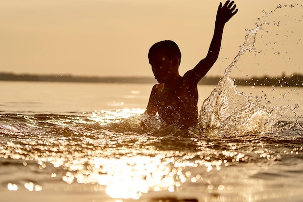 Bambino che gioca in acqua Spruzza intorno al ragazzo nel fiume Bel tramonto Vacanze estive e concetto di infanzia Ragazzino che si diverte Primo piano