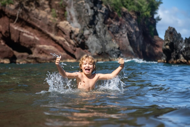 Bambino che gioca nell'acqua dell'oceano bambino che salta nelle onde del mare vacanza per bambini sulla spiaggia piccolo ragazzo eccitato