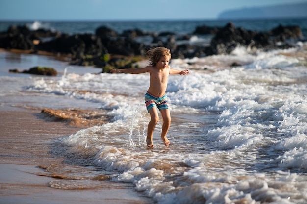 Bambino che gioca sulla spiaggia dell'oceano bambino che salta tra le onde in vacanza in mare ragazzino che corre sul tropicale...