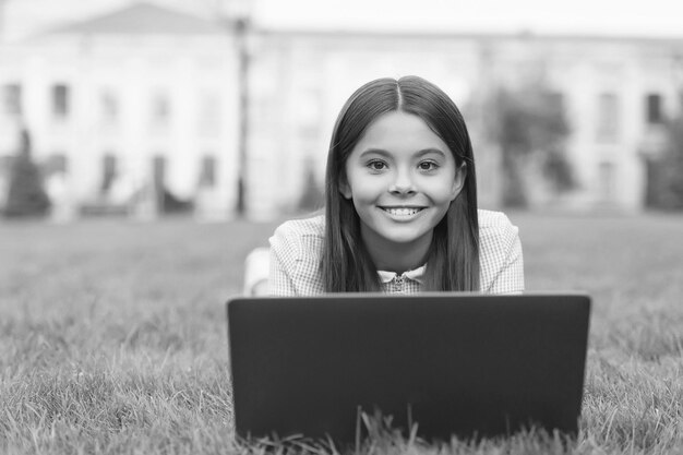 Bambino che impara lezione privata blogging ragazza felice seduta sull'erba verde con il laptop Avvia il bambino che gioca al computer torna a scuola istruzione online giornata della conoscenza Divertirsi