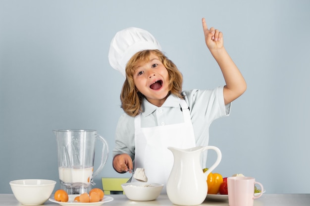 Bambino che indossa uniforme da cucina e cappello da chef che prepara il cibo con farina su cucina ritratto in studio cooki