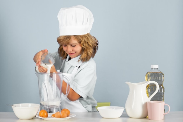 Bambino che indossa uniforme da cucina e cappello da chef che prepara le verdure sul ritratto dello studio della cucina che cucina cu