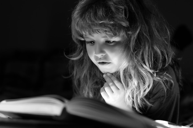 Bambino che legge un libro a letto prima di andare a dormire ragazzino sdraiato sul letto leggendo un libro a casa conce