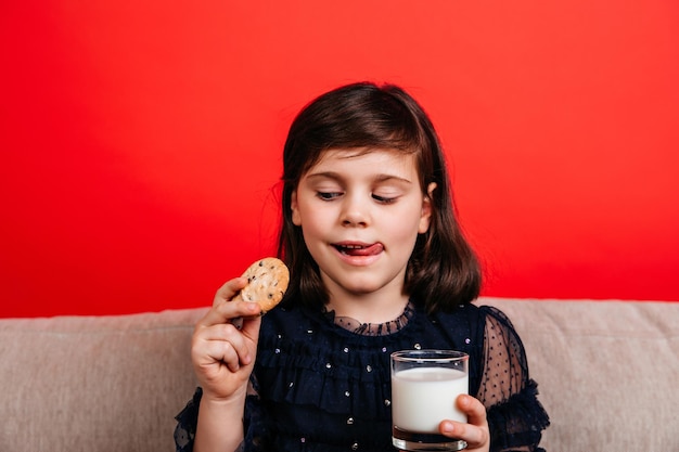 Bambino che mangia biscotto con piacere Bambino che beve latte su sfondo rosso