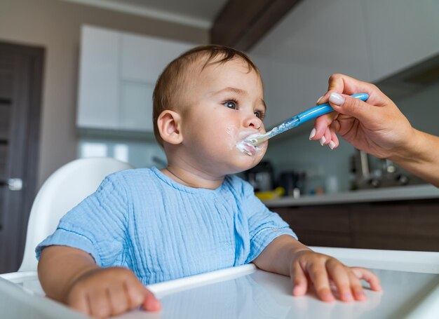 Bambino che mangia cibo in cucina Madre che allatta il bambino con il cucchiaio al chiuso