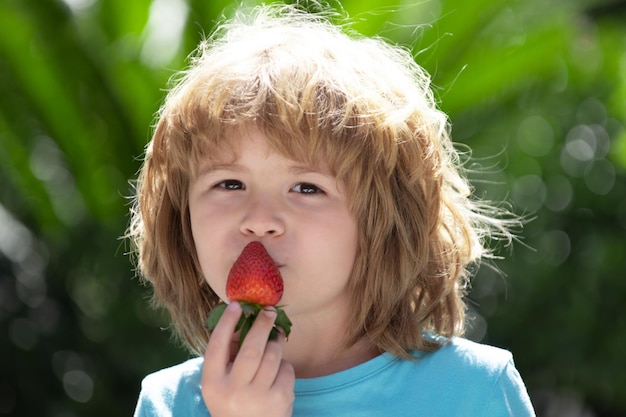 Bambino che mangia fragola su sfondo verde estivo.